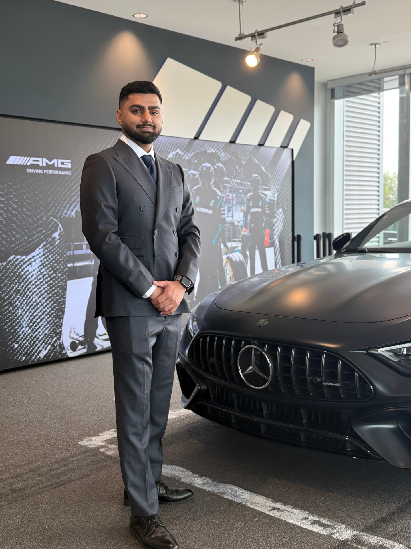 Client in a charcoal grey pinstripe double-breasted suit beside a Mercedes-AMG in a showroom