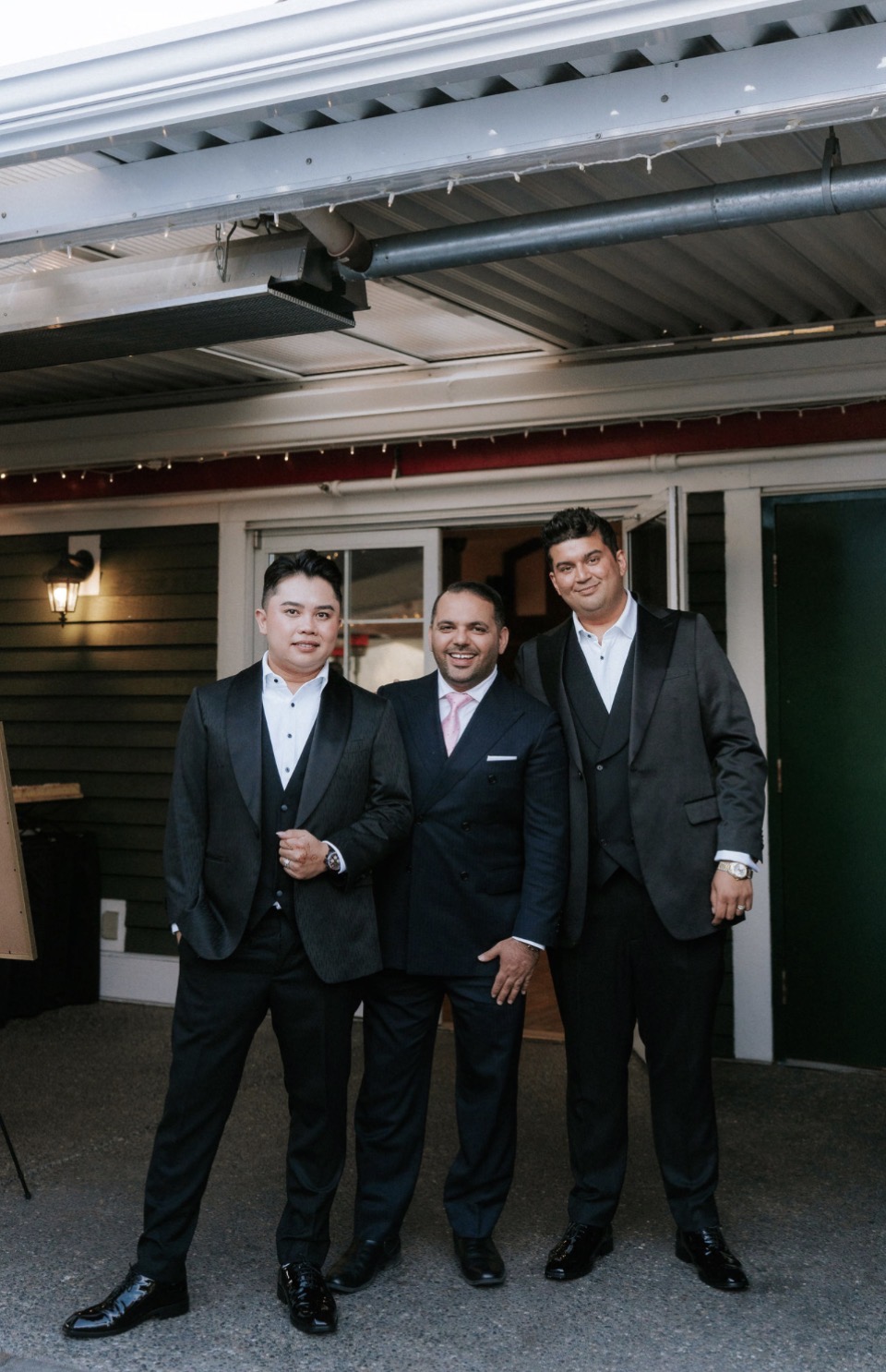 Three men in formal evening wear — two grooms in jacquard tuxedos and the tailor in a wool blend pinstripe suit