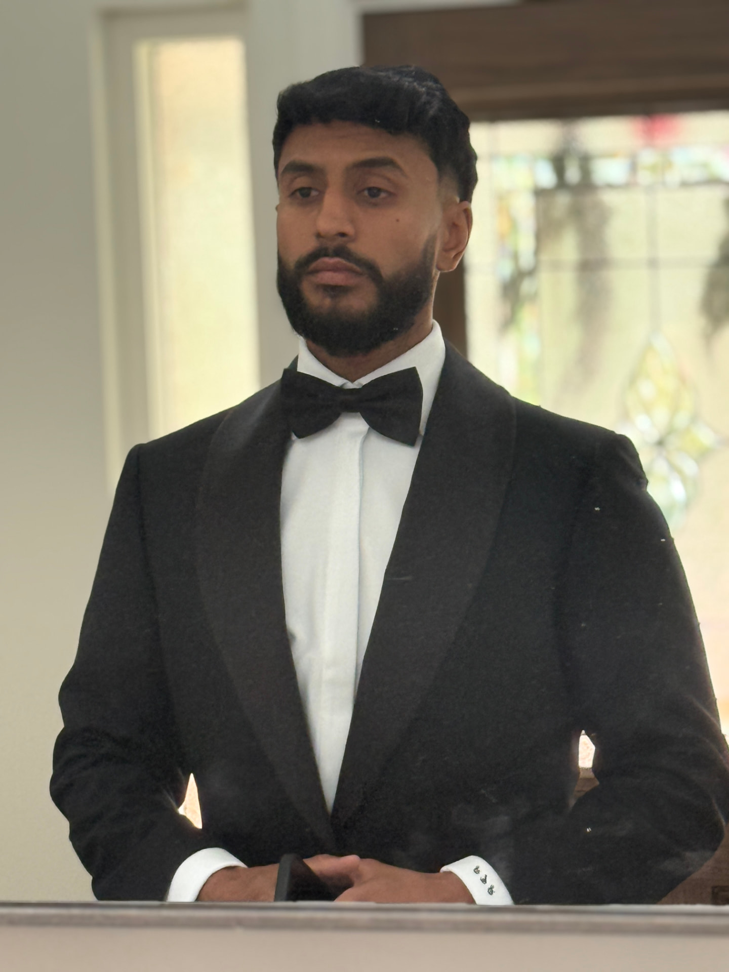 Groom in a black shawl-lapel tuxedo with a satin bow tie, standing in warm indoor light